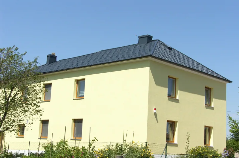 Gelbes zweistöckiges Haus mit anthrazitfarbenem Prefa-Walmdach