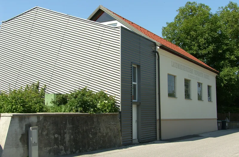 Halle mit grauer Trapezblechfassade neben einem alten Werkstattgebäude