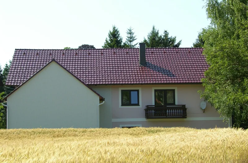 Haus mit dunkelrotem Ziegeldach hinter einem Getreidefeld