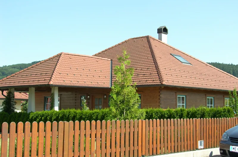 Haus mit rotem Ziegel-Walmdach hinter einem Holzlattenzaun