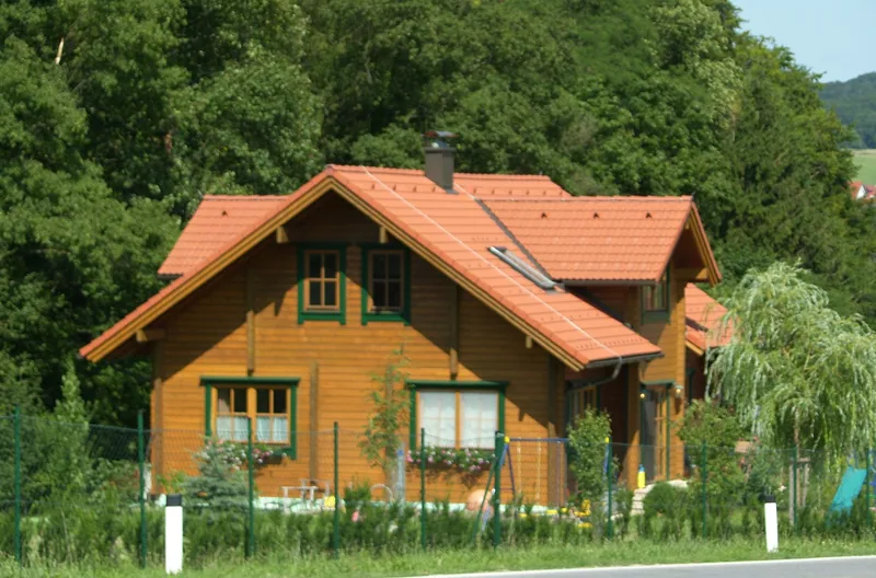Holzhaus mit orangem Dach aus Bramac-Classic-Steinen vor einem Waldrand